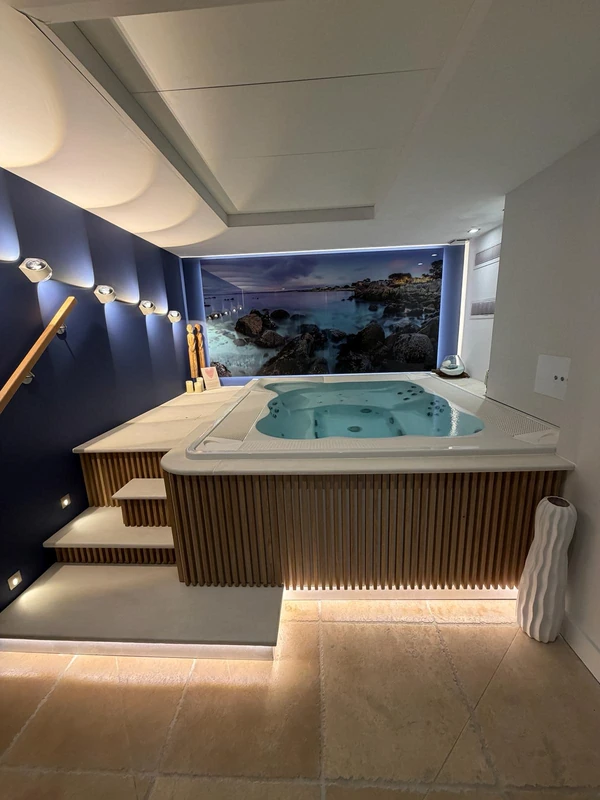 Spa Jacuzzi® encastré dans l'espace détente d'un institut professionnel, avec escalier en bois et éclairage indirect